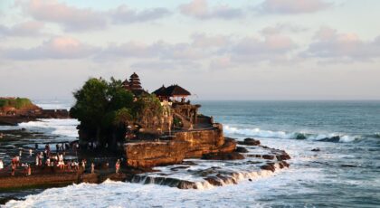 Scenic aerial view of the iconic Tanah Lot Temple on the coast of Bali, surrounded by waves.