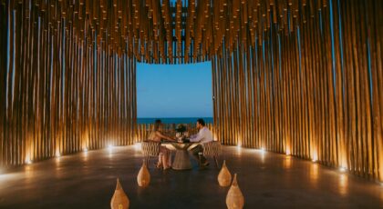 A couple enjoys a romantic dinner in a stylish oceanfront pavilion at twilight.