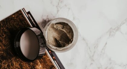High-angle view of a clay mask in a glass jar on a marble surface with a magazine.