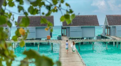 Romantic couple walking hand in hand on a wooden boardwalk with overwater villas in the Maldives.