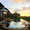 A serene view of a villa's infinity pool at sunset in Bali, Indonesia, with lush greenery and calm reflections.