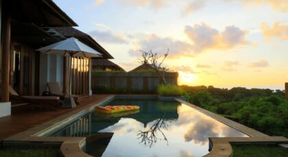 A serene view of a villa's infinity pool at sunset in Bali, Indonesia, with lush greenery and calm reflections.