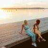 Two women enjoying a peaceful sunset on a lakeside jetty, embracing outdoor tranquility.