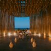 A couple enjoys a romantic dinner in a stylish oceanfront pavilion at twilight.
