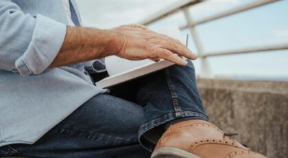 A senior man reading a book outdoors on a sunny day, relaxing in casual attire.