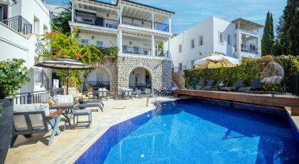 Lavish villa in Bodrum with poolside seating and vibrant greenery under a sunny sky.