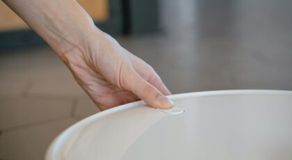 A close-up of a hand gently holding the white lid of a kitchen pot.