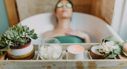 Woman relaxing in a bathtub with a candle and plants, enjoying a serene spa experience.