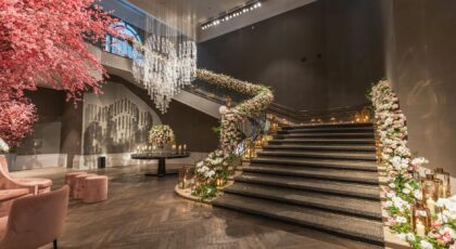An opulent indoor staircase beautifully decorated with flowers, chandelier, and ambient lighting.
