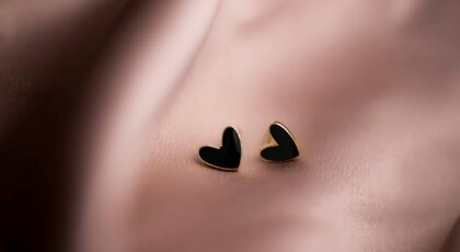 Chic black heart-shaped earrings with golden edges resting on silky pink fabric, ideal for fashion and elegance themes.