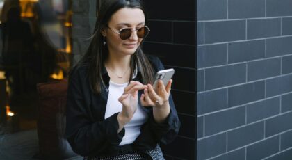 Trendy woman with sunglasses using a smartphone outdoors. Urban lifestyle captured in a candid moment.