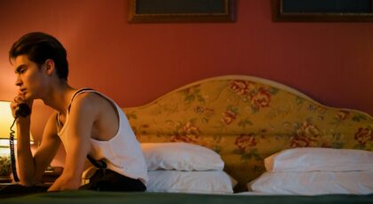 Young man seated on bed with retro floral headboard, using a vintage phone in a cozy room.