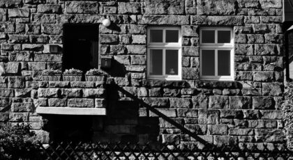 Black and white image of a rustic stone house facade with classic architecture and a fenced entrance.
