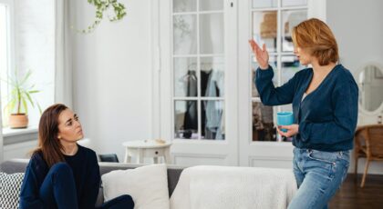 Two women engage in a friendly chat in a stylish living room, one sitting and one standing with a mug.