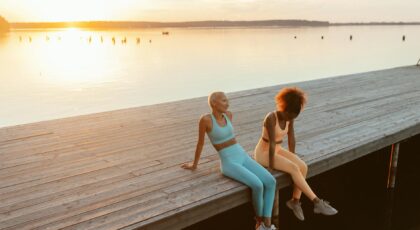 Two women enjoying a peaceful sunset on a lakeside jetty, embracing outdoor tranquility.