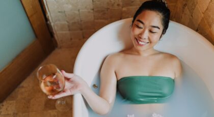 Asian woman enjoying a relaxing bath with wine and flowers, embodying spa-like wellness and tranquility.
