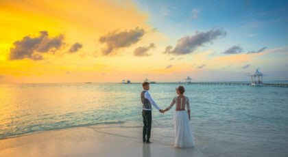 A romantic couple holding hands at sunset on a Maldives beach, exuding love and tranquility.