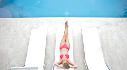 Woman in a bikini relaxing on a sun lounger by a poolside during summer.