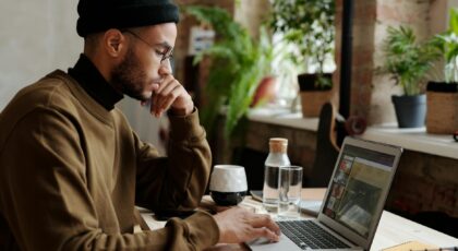 A stylish young man works remotely on his laptop in a cozy indoor workspace.